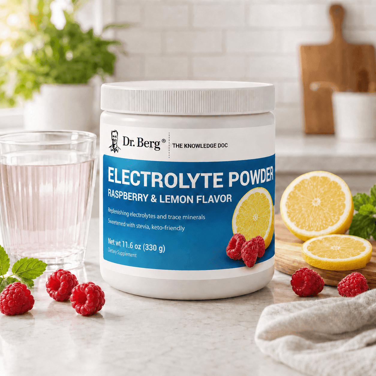 A tub of Dr. Berg Electrolyte Powder, raspberry and lemon flavor, on a kitchen counter beside a glass of pink drink, fresh raspberries, and lemon