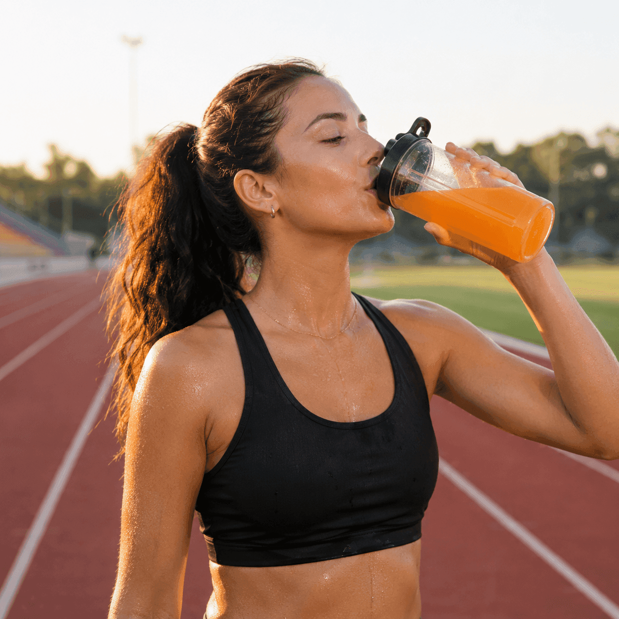 An athlete in workout clothes drinking an orange beverage from a bottle on a running track