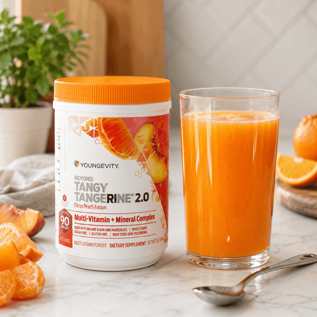 A container of Beyond Tangy Tangerine 2.0 next to a tall glass of bright orange drink, with oranges and a spoon on a marble counter